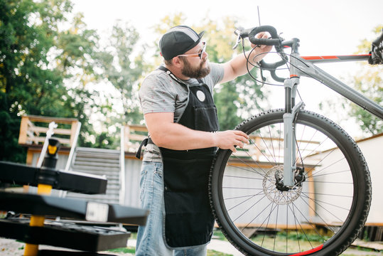 Bicycle mechanic in apron adjusts bike outdoor