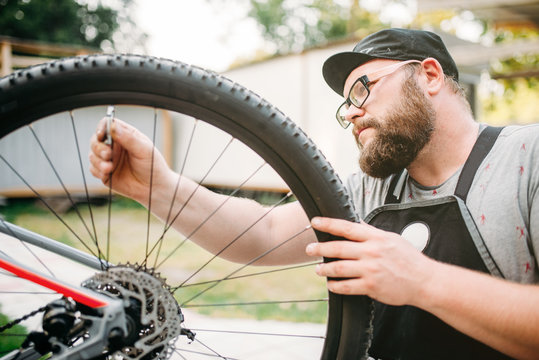 Bicycle mechanic in apron adjusts bike spokes