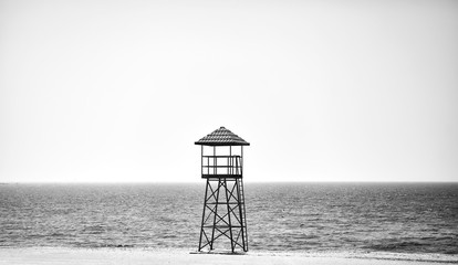 Black and white picture of a lifeguard tower on an empty beach. 