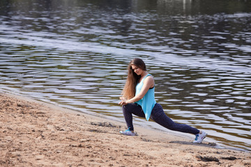 A girl with long hair trains on the sand near the water.