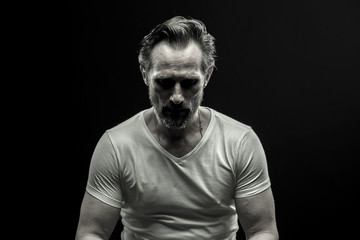 Black and white portrait of mid aged man. Male in white t-shirt on black background showing emotion...