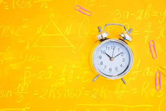 back to school or office styed scene with alarm clock and copy space on yellow background with math formulas
