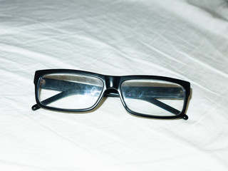 folded up black glasses resting on white bed sheet