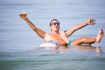 Handsome man swimming on rubber ring in sea with glass of beer and party mood enjoy summer vocation