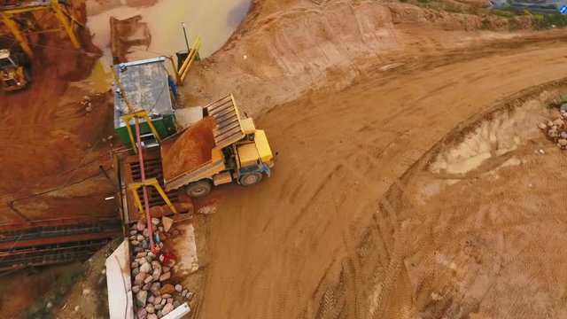 Mining truck transporting sand to sorting conveyor belt. Mining machinery in industrial area at sand quarry. Mining equipment. Mining industry. Dump truck. Heavy vehicle