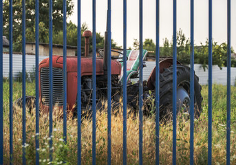 Fototapeta premium Red old tractor behind a blue fence