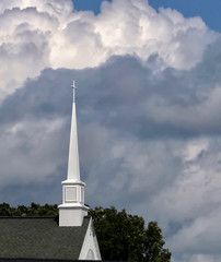 A white church steeple against blue puffy clouds