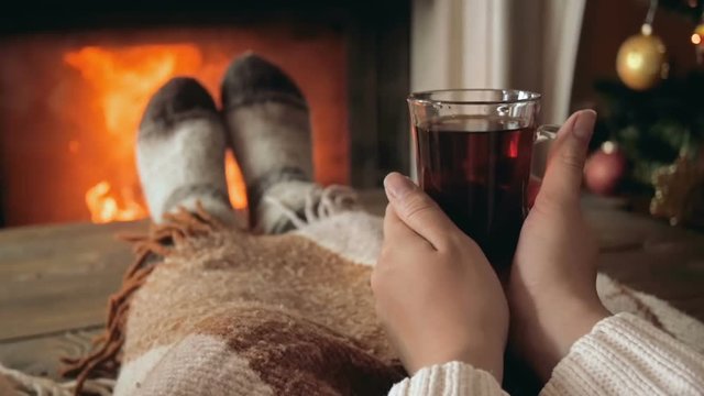 Closeup slow motion video of young woman warming at fireplace with cup of tea