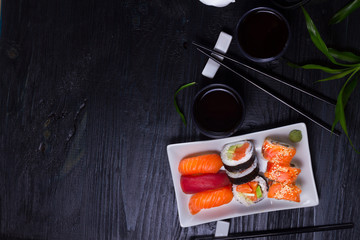 Japanese sushi dish with tea and chopsticks on black wooden background with copy space