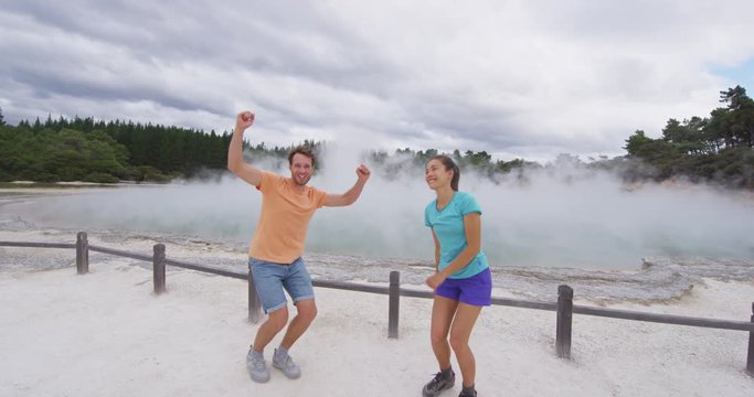 New Zealand happy tourist couple jumping happy having fun at famous attraction travel destination. Champagne pool, Waiotapu. Active geothermal area, in Taupo Volcanic Zone, Rotorua, New Zealand.