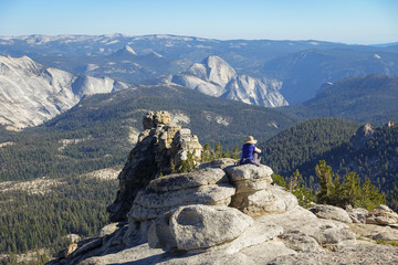 A lone woman sits looking out over Half Dome and Valley, in Yosemite National Park.