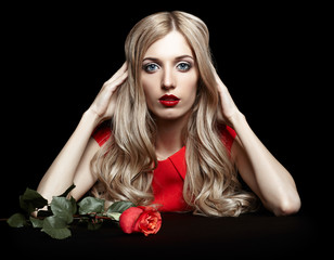 Portrait of young beautiful blonde woman in red dress with red rose in hands on black