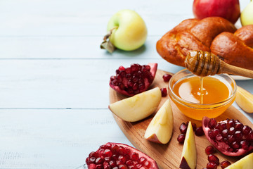 Honey, apple slices, pomegranate and hala serve on wooden kitchen board. Table set with traditional food for Jewish New Year Holiday, Rosh Hashana. Copy space for text. - obrazy, fototapety, plakaty