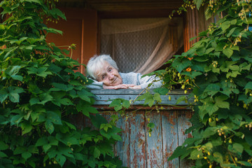 An elderly woman in the veranda among the greenery.