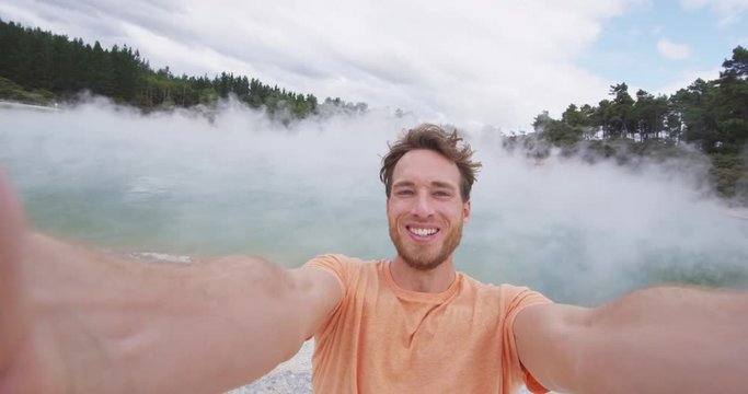 Tourists man taking selfie at New Zealand Waiotapu pools travel destination. Young traveller having fun sightseeing at colorful geothermal hot springs ponds, Waiotapu, Rotorua, New Zealand.