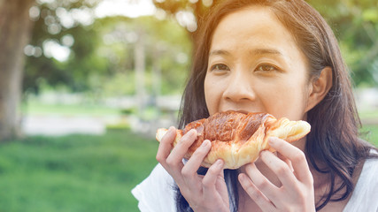 Asian woman holding and eating fresh baked bakery in green background park