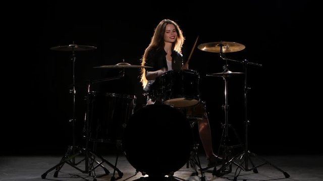 Drummer girl starts playing energetic music, she smiles. Black background