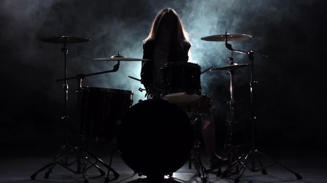 Specially trained girl plays the drums. Black smoke background. Silhouette. Slow motion