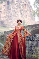 Beautiful Isabella of France, queen of England on Middle Ages period in red gown near medieval castle