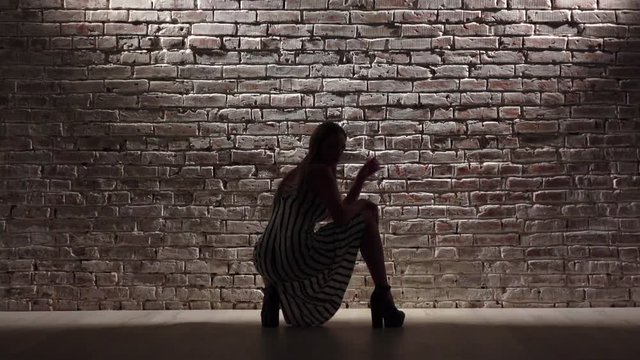 Elegant tall woman in high heels dance twerk against a brick wall. Silhouette. Slow motion