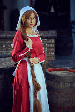 Townswoman in red dress with an apron and chaperone on the street. Costume stylized of later Middle Ages on 15/ 16th century.