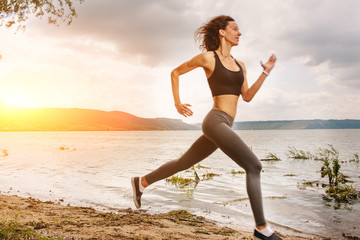 A beautiful sporty woman runing on the shore of a lake in sportswear. Girl is exercising