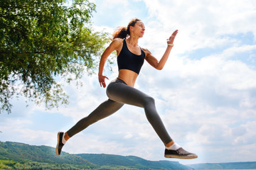 Fototapeta premium A beautiful sporty woman runing on the shore of a lake in sportswear. Girl is exercising