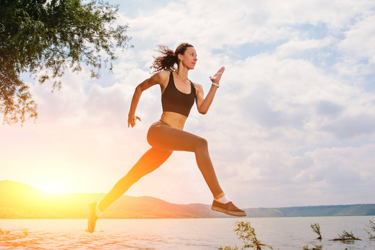 A beautiful sporty woman runing on the shore of a lake in sportswear. Girl is exercising