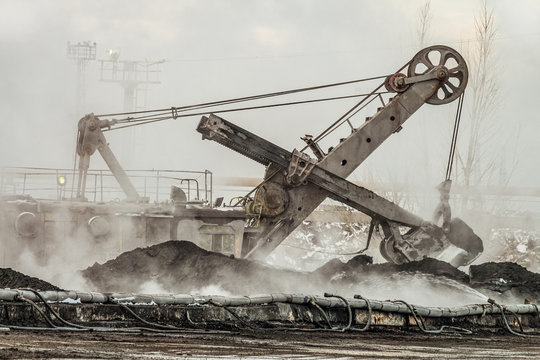 large bucket excavator works in a hot outdoors dump. Heavy industrial metallurgical foggy landscape