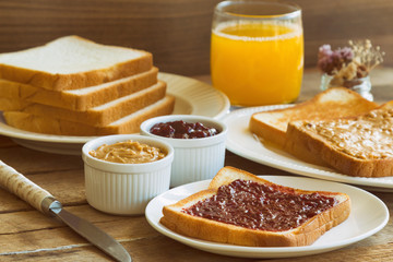 Fototapeta na wymiar Toast bread with homemade strawberry jam and peanut butter served with orange juice. Homemade toast bread with jam and peanut butter on wood table for breakfast. Delicious toast bread ready to served.