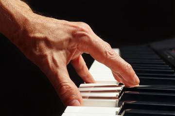 Hand of pianist play the keys of the electronic synth on a black background close up