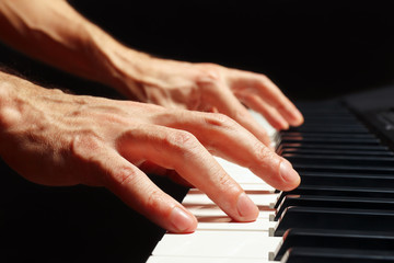 Hands of composer play the keys of the piano on a black background close up