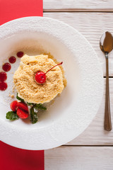 Napoleon cake serving on contrast red and white background. Sweet dessert on plate with decoration from strawberry, cherry and mint, close up top view