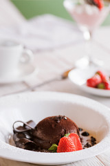 Chocolate fondant on white plate with decoration from strawberry and mint. Delicious dessert serving in restaurant, close up