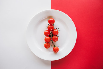 Conceptual picture of fresh cherry tomatoes on plate. Healthy ripe vegetables on contrast white and red background, top view