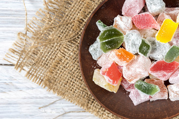 Multicolored sweets, marmalade on a clay plate. Background of burlap. Rustic style.
