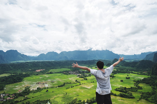 a man raising hand up on mountain peak, traveling in tropical countryside, Vang Vieng in Laos