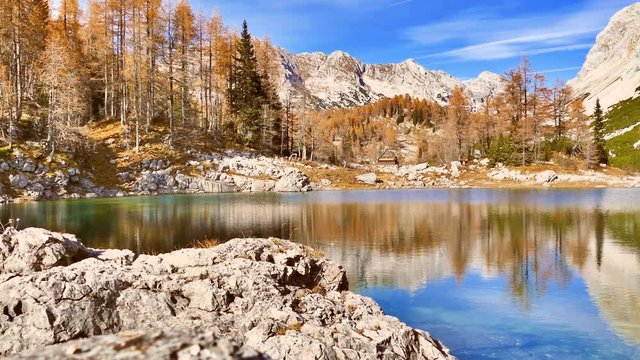 Mountain hut by Alpine lake in autumn season. Pan right, UHD.
