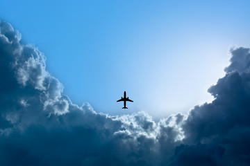 Silhouette airplane flying in blue sky with rain clouds and sunshine