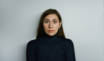 Picture of funny emotional bug-eyed brunette girl of European appearance looking at camera, having shocked amazed expression on her pretty face. Human emotions, feelings, reaction and attitude