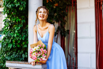 girl in a blue dress with a bouquet standing near white column