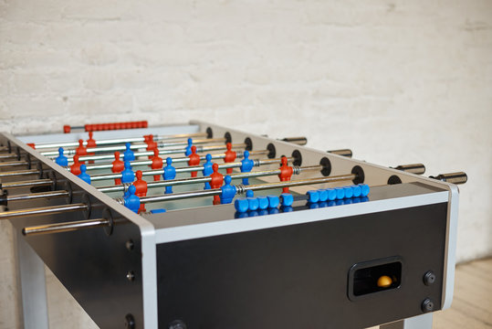 Detailed close up picture of foosball table with metall rods with red and blue foos men players figures in empty room with white blank copyspace wall for your advertisement or promotional content