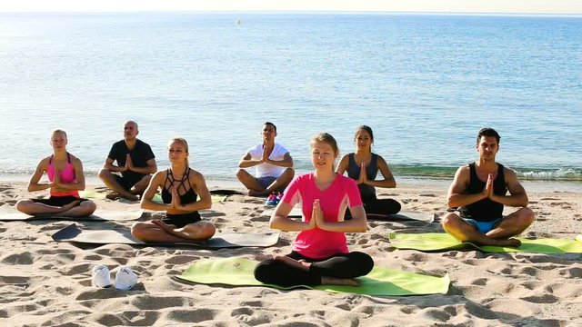 Sporty females and males meditating in yoga position Padmasana on seaside
