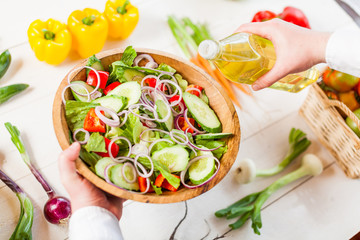 man pouring olive oil into healthy salad on kitchen