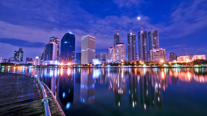 Fototapeta premium Night light cityscape view with modern building in the park beside lake at Bangkok, Thailand (Blue color tone)