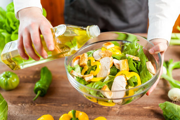 man pouring olive oil into healthy chicken salad on kitchen