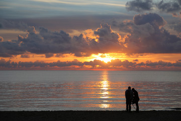 Two unidentifiable people watching sunset over the sea