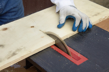 Ręce robotnika w rękawicach ochronnych trzymają deskę i tną deskę na pile stołowej.