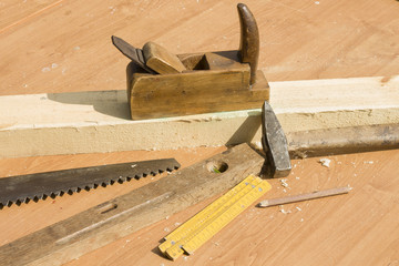 Stary hebel stoi na stole. Narzędzia stolarskie piła i wióry leżą na stole.