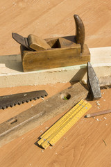 Stare narzędzia stolarskie leżą na stole. Hebel, piła, poziomnica, miarka, młotek, ołówek,